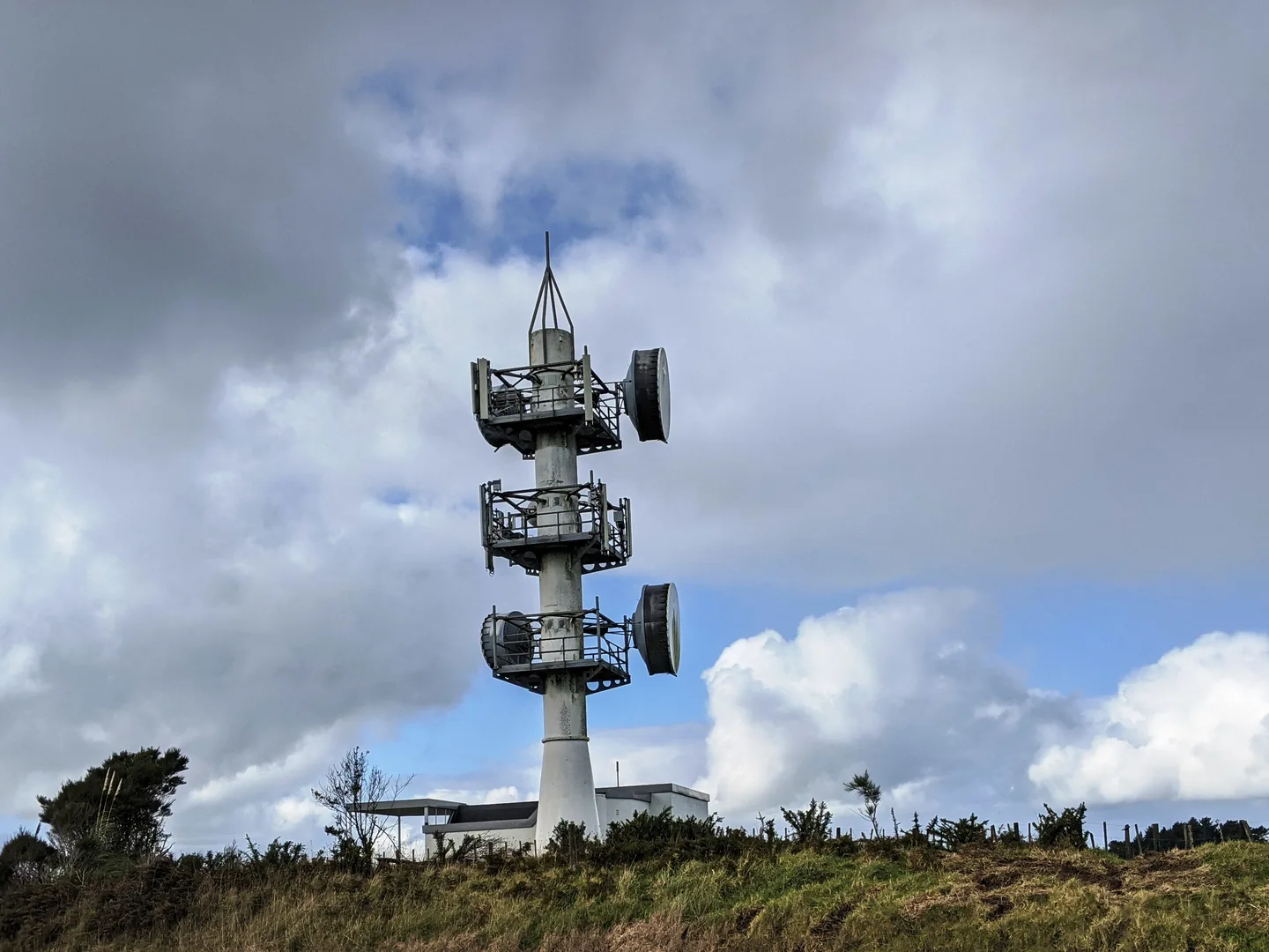A telecommunications tower with equipment platforms and microwave dishes under a clouded sky